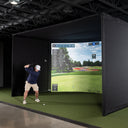 Golfer mid swing in an indoor simulator bay with the course projected across the screen