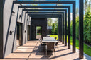 Covered pergola terrace with an outdoor dining table alongside a modern home