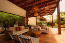 Covered wooden patio with sofas and lounge chairs surrounded by tropical plants