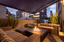 City rooftop terrace with a fire pit table and wicker sofas at dusk