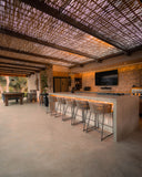 Covered outdoor bar with stools, stone wall and TV under a woven pergola
