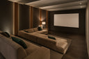 Contemporary home theater with a wide projection screen, deep sectional seating and warm architectural lighting